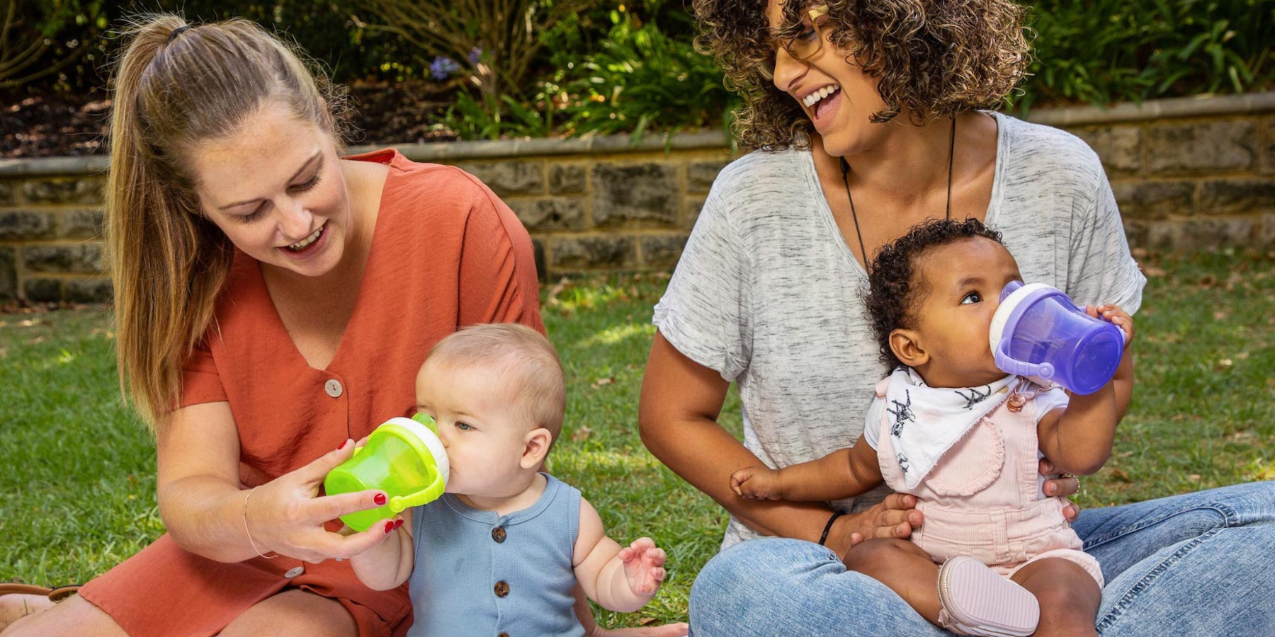 two mother and babies using "A v sippy cup called 'The One Cup' that converts into a straw cup and snack cup. It features a retractable lid for easy storage, removable handles for customizable grip, and a soft silicone spout and straw for gentle sipping. 