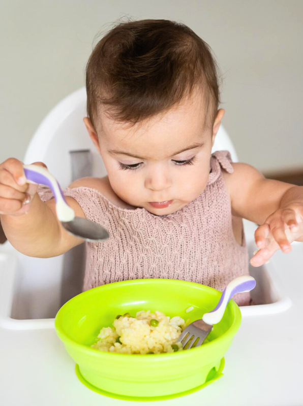 a toddler using an ergonomic training fork and spoon set .  utensils feature curved, over-molded handles for increased softness and added grip, making it . The stainless-steel fork tines and spoon bowl are perfectly sized for small mouths, with the fork having rounded prongs for safety and the spoon featuring a shallow bowl for easy scooping. 